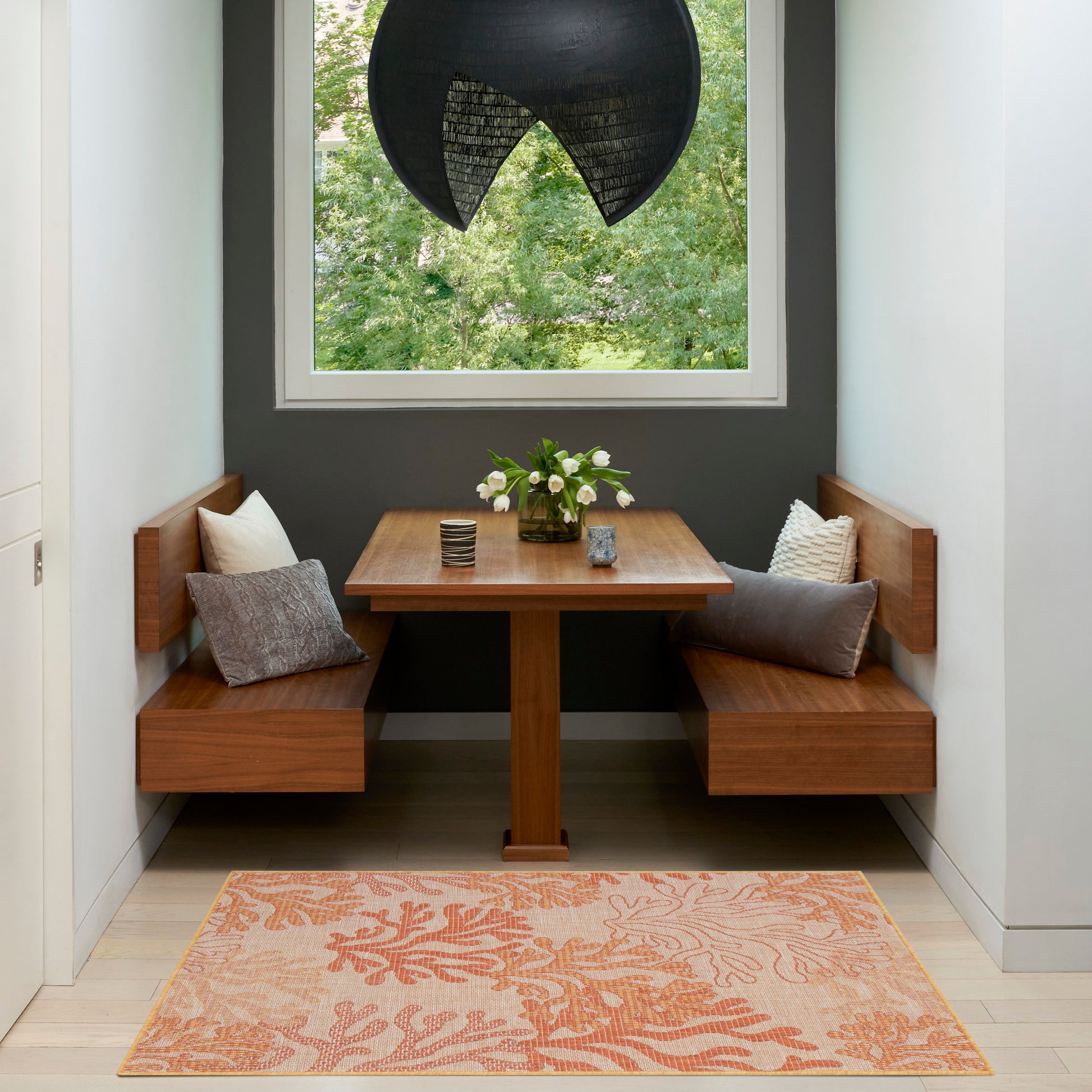 Cozy wooden dining nook with benches, square table, gray walls, peach rug, black pendant lamp, floral centerpiece.
