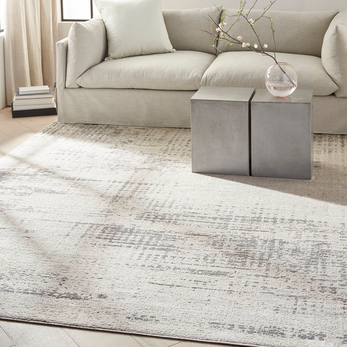 Neutral living room with beige sofa, textured cream rug, concrete block side tables, and vase with blossom branches.