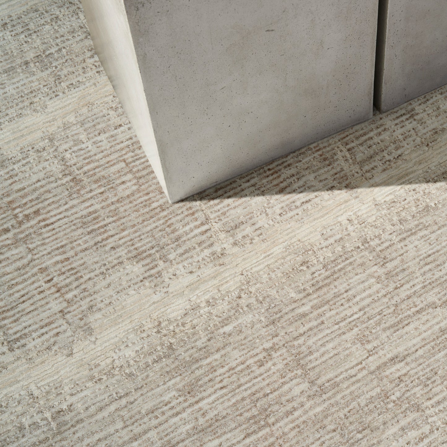 Beige textured carpet with subtle linear stripes beside a light gray concrete block corner.