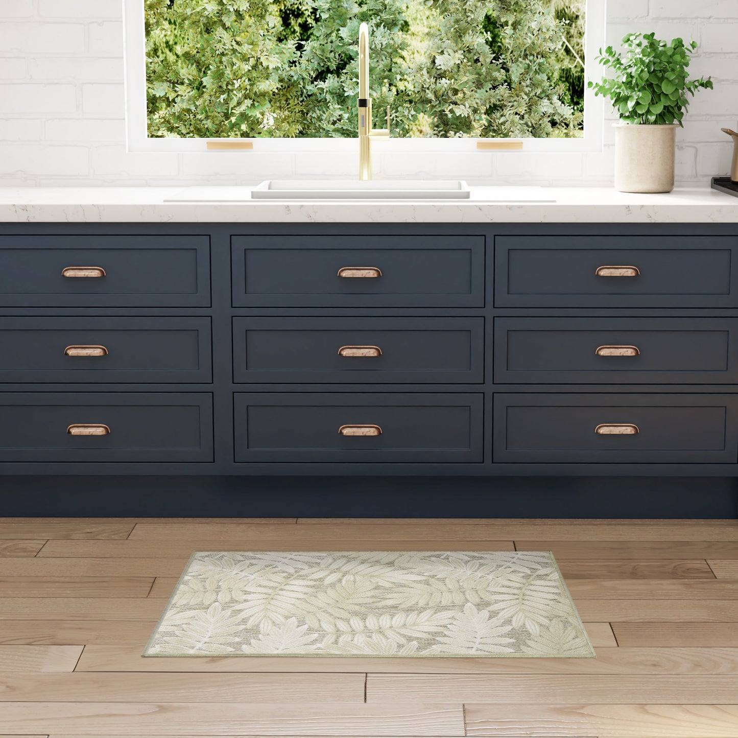 Dark navy kitchen drawers with brass handles, white countertop and gold faucet; mint leaf-pattern rug on wood floor.