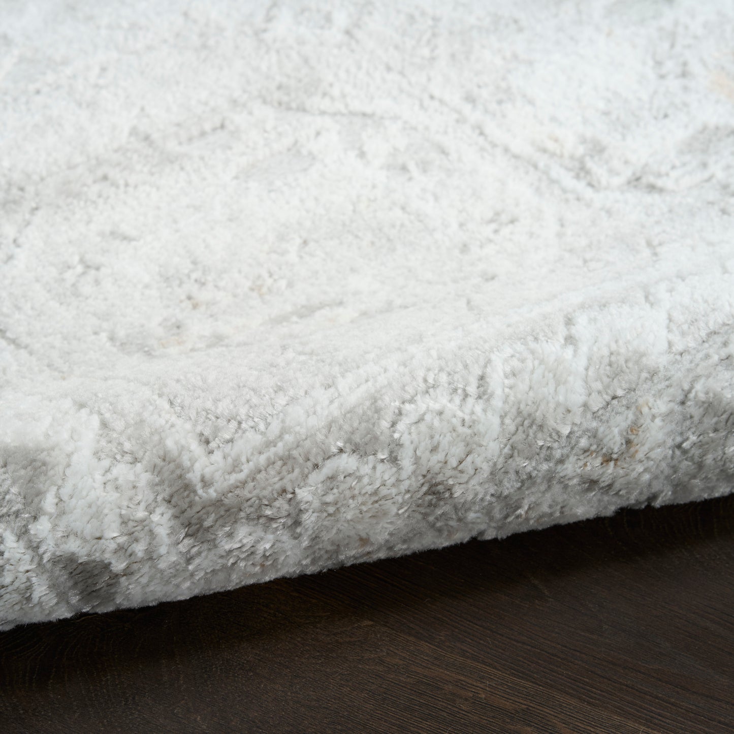 White plush shag rug with thick fur-like pile on dark hardwood floor.