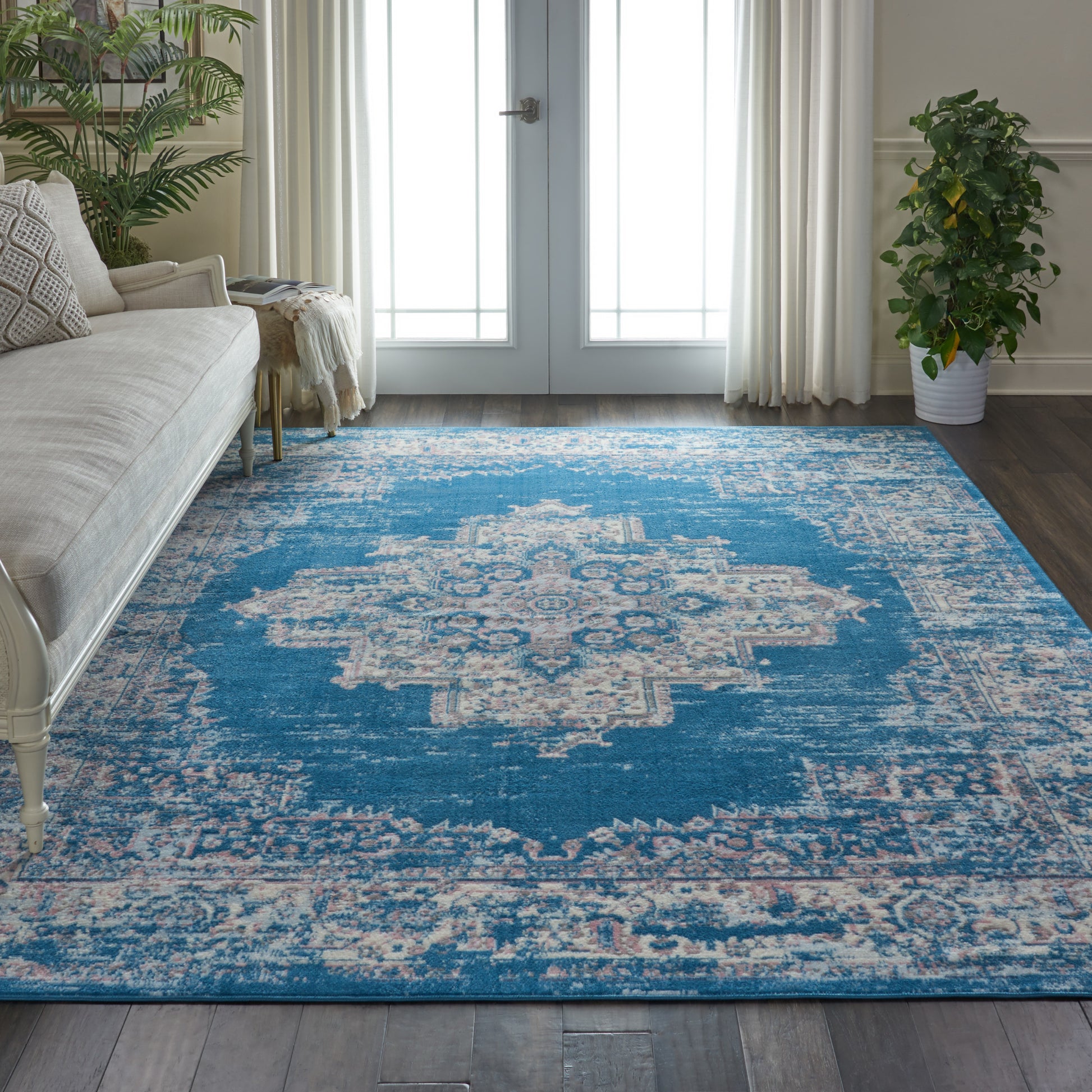 Blue vintage medallion area rug in cream and teal, in a bright living room with beige sofa and potted plants.
