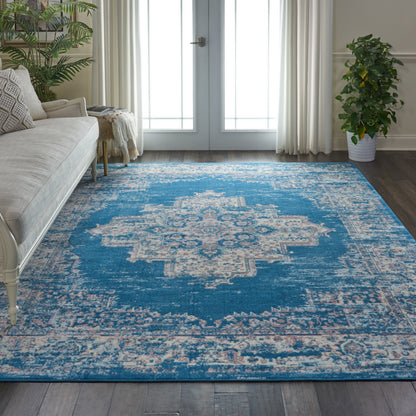 Blue vintage medallion area rug in cream and teal, in a bright living room with beige sofa and potted plants.