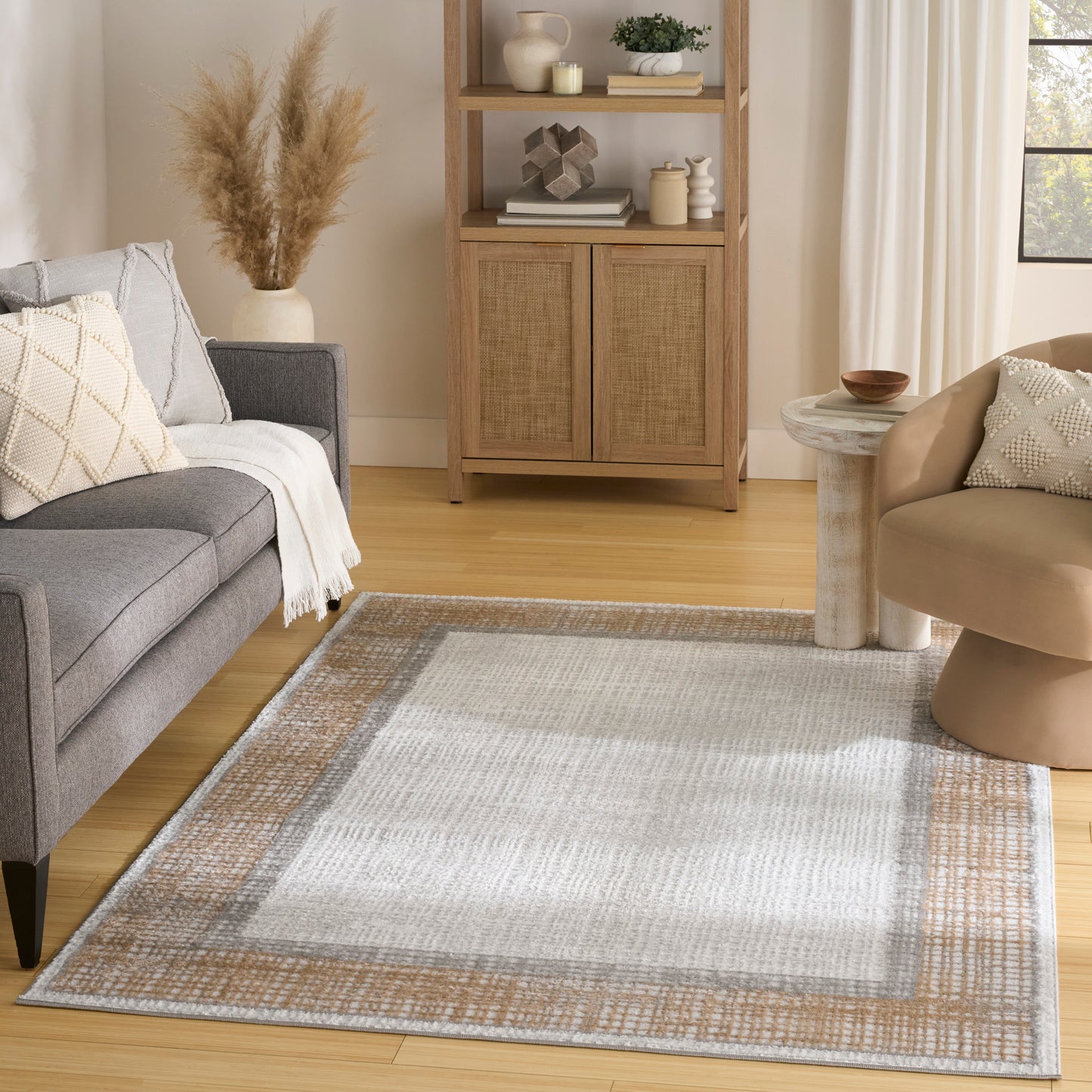 Neutral living room with gray sofa, beige chair, tan-border woven rug, and wooden cabinet with woven doors.