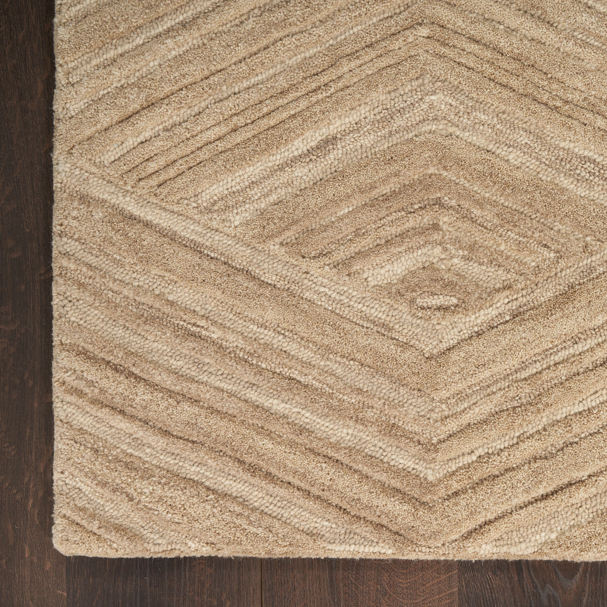 Beige textured rug with chevron diamond pattern on dark wood floor.