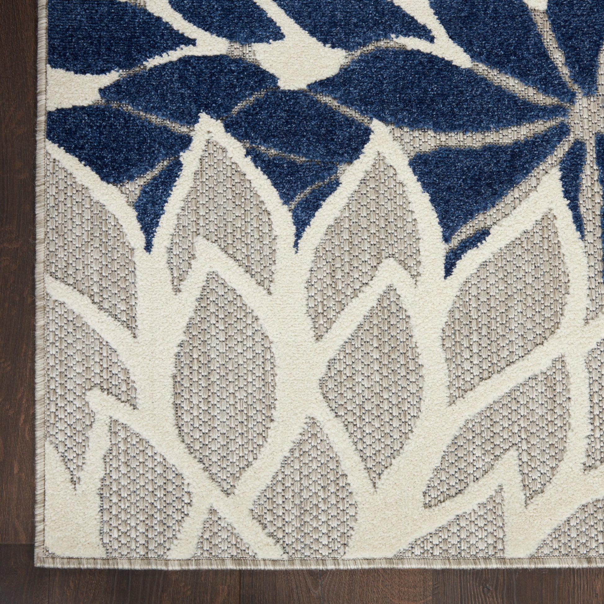 Woven rug with navy blue botanical leaf motif on ivory-beige field; dark brown edge, on wood floor.
