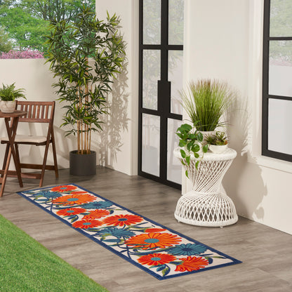 Floral runner rug with orange, blue and red blossoms on cream background with navy border, on wood floor beside glass doors.