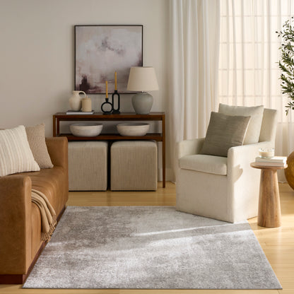 Neutral living room with tan leather sofa, cream armchair, gray rug, wooden console, lamps, & abstract art.