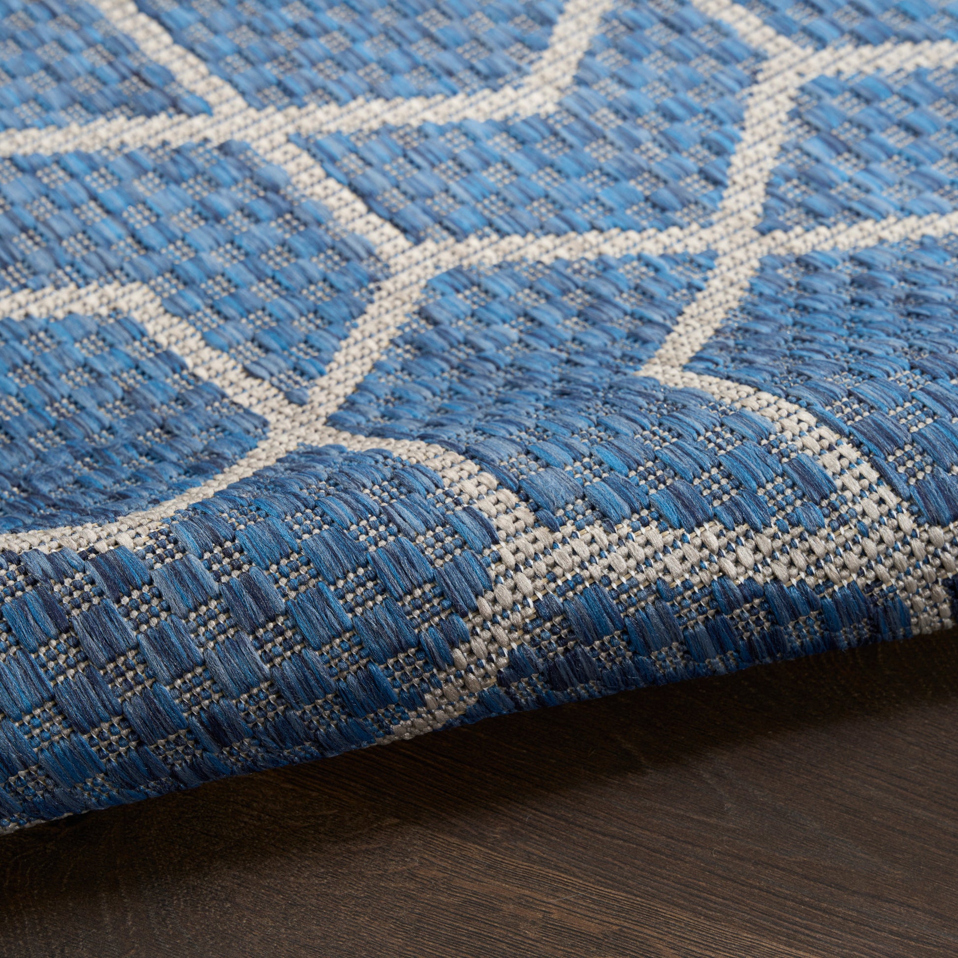 Blue and cream geometric woven rug with lattice pattern, textured flatweave on dark wood floor.
