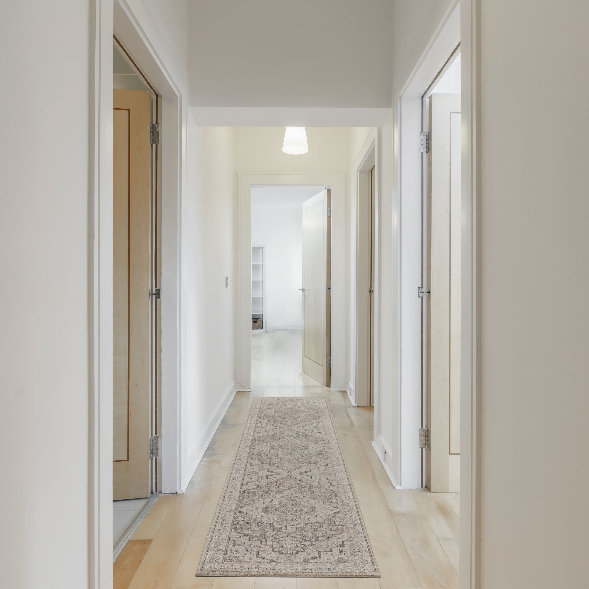 Bright hallway with white walls, light wood doors, a beige patterned runner rug, and a pendant ceiling light.