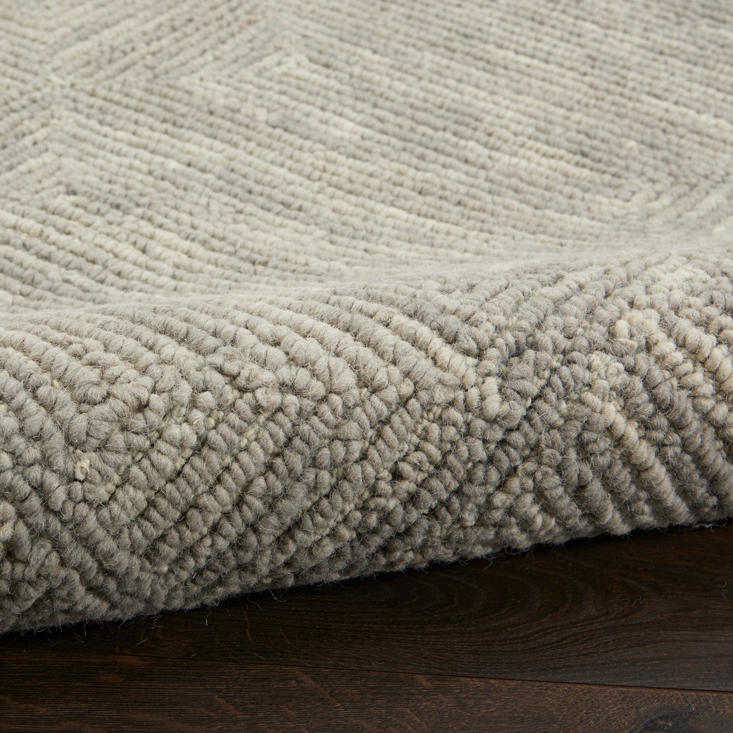 Cream-gray plush area rug with thick looped pile and subtle geometric pattern on dark wooden floor.