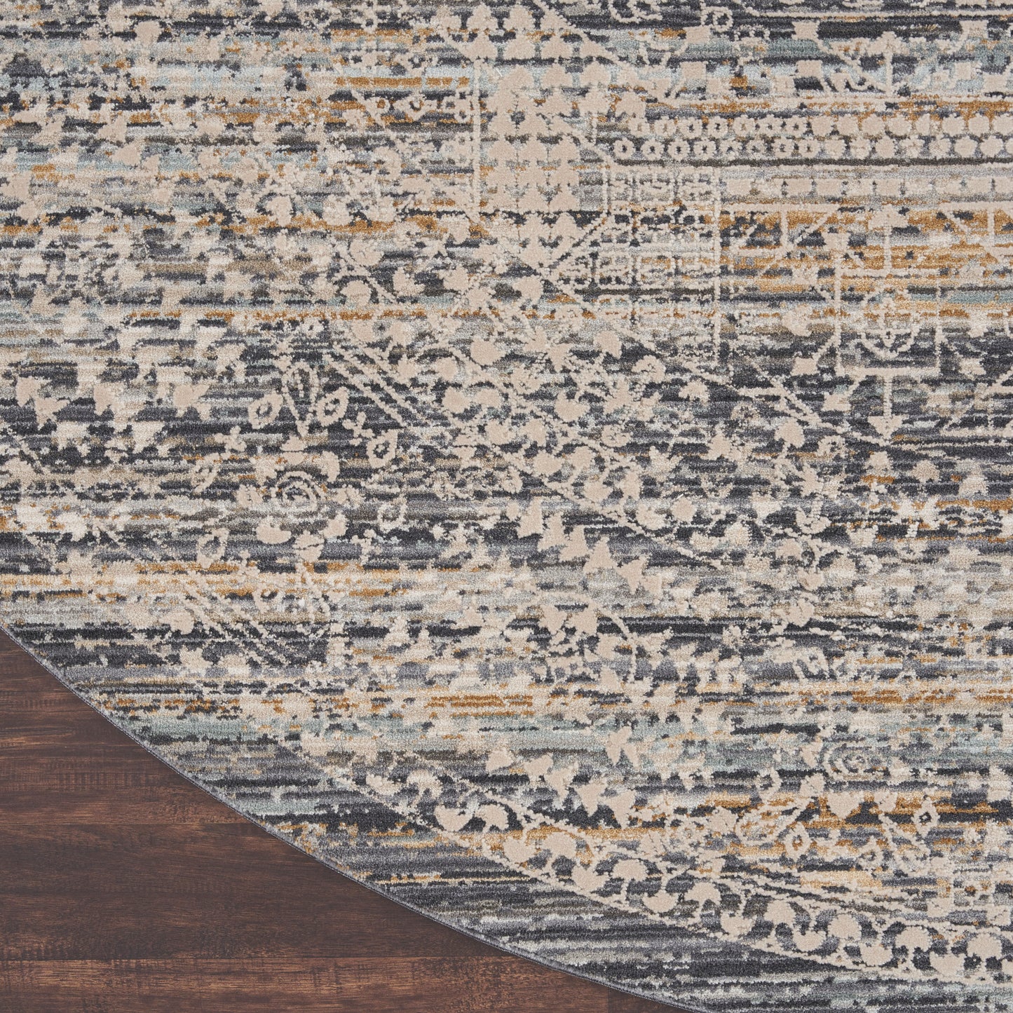 Round distressed oriental rug in blue, gray, cream & tan with vintage floral motifs on dark wood floor.