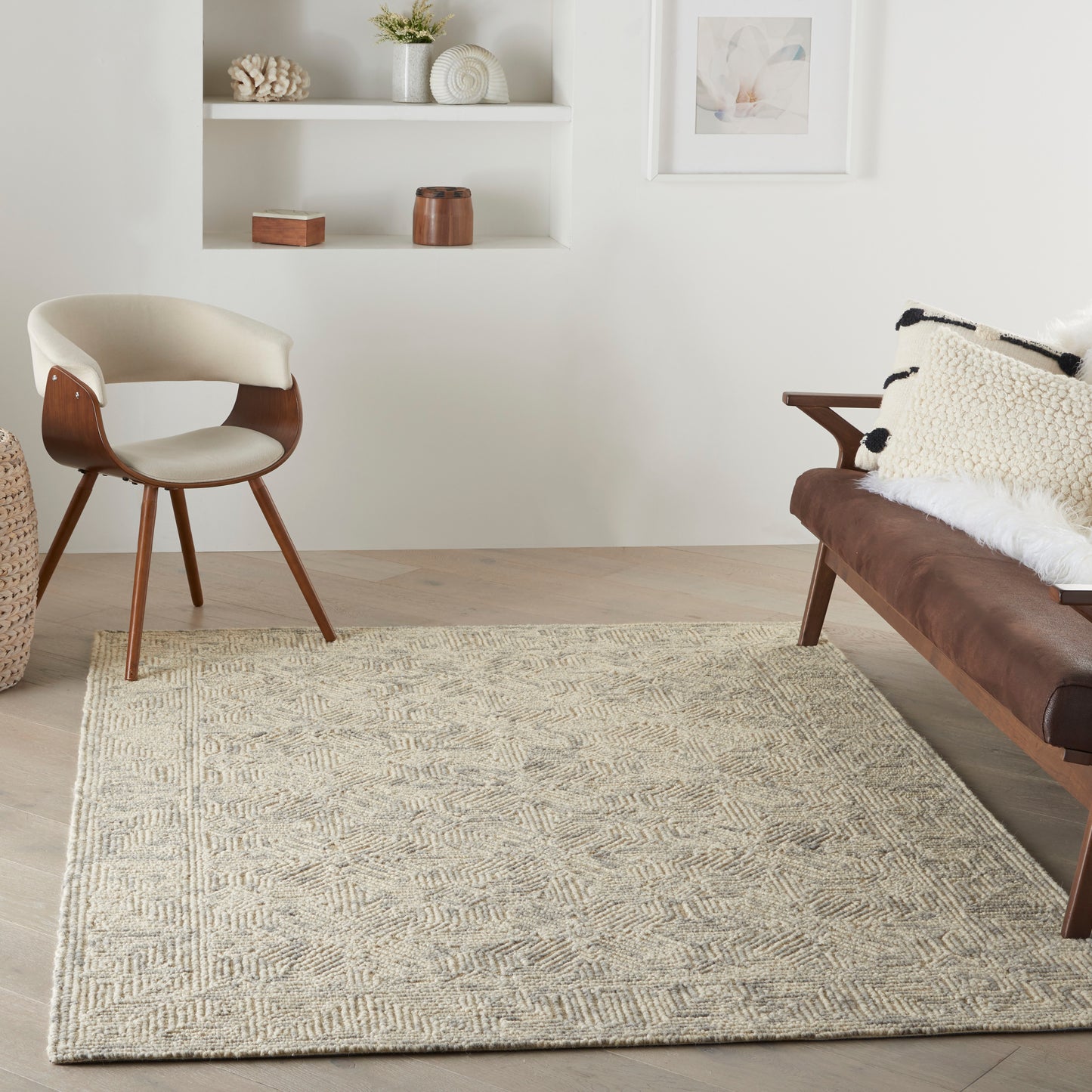 Cozy mid-century living room with a beige patterned rug, cream chair, brown leather sofa, and white wall shelves.