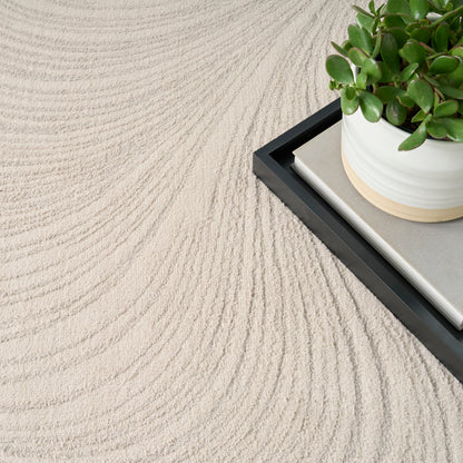 Beige textured rug with concentric wave patterns; black tray holds a white pot with a green succulent on a beige book.
