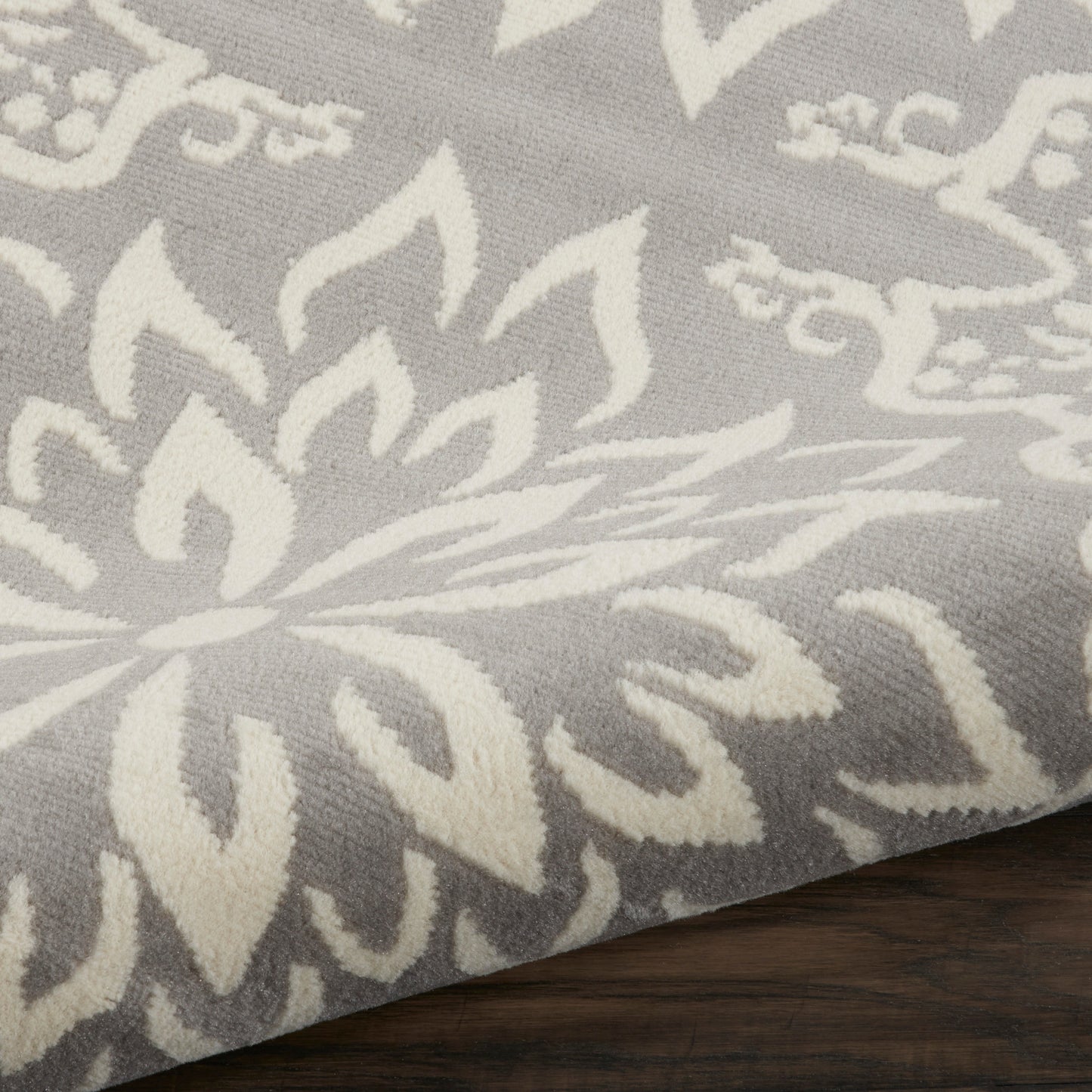 Grey fabric with white damask floral pattern, soft woven textile draped over dark wood surface.
