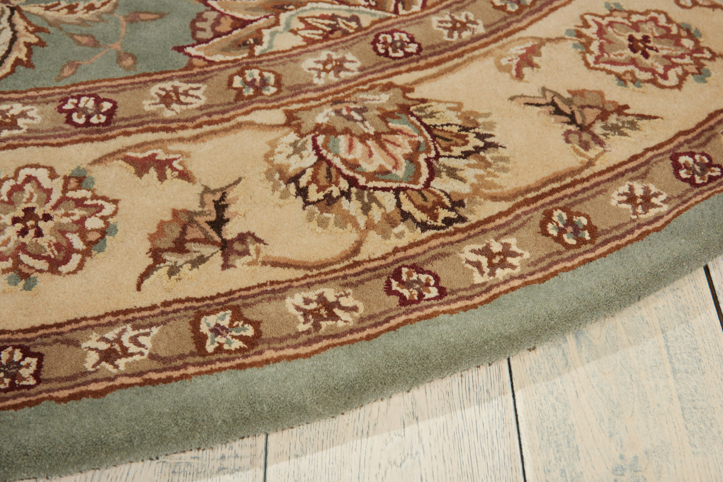 Round oriental-style area rug with beige field, brown floral motifs and teal border on light wood floor.