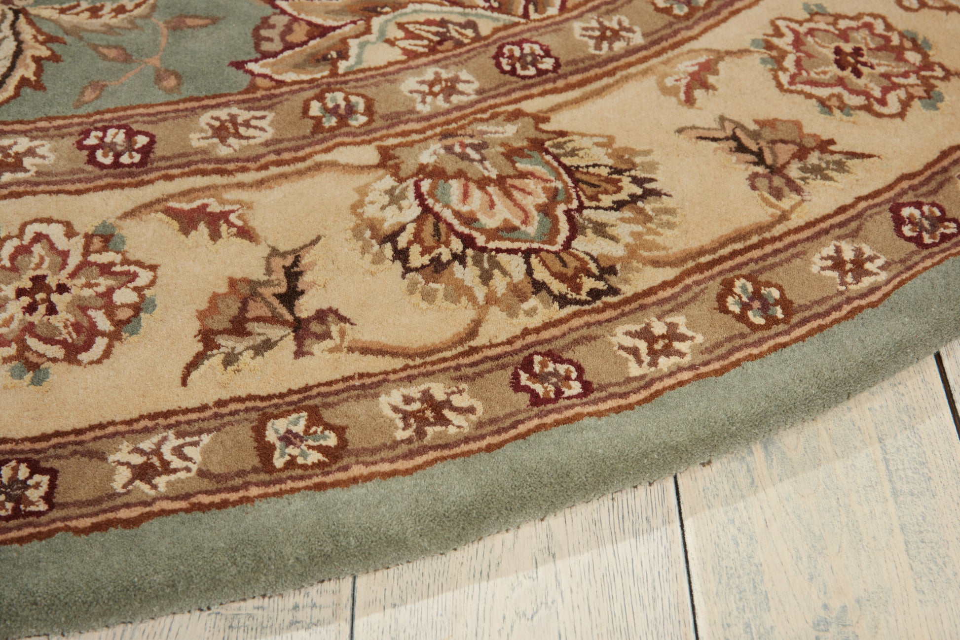 Round oriental-style area rug with beige field, brown floral motifs and teal border on light wood floor.
