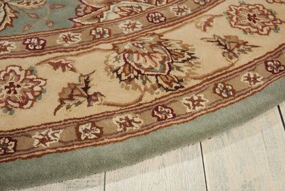 Round oriental-style area rug with beige field, brown floral motifs and teal border on light wood floor.