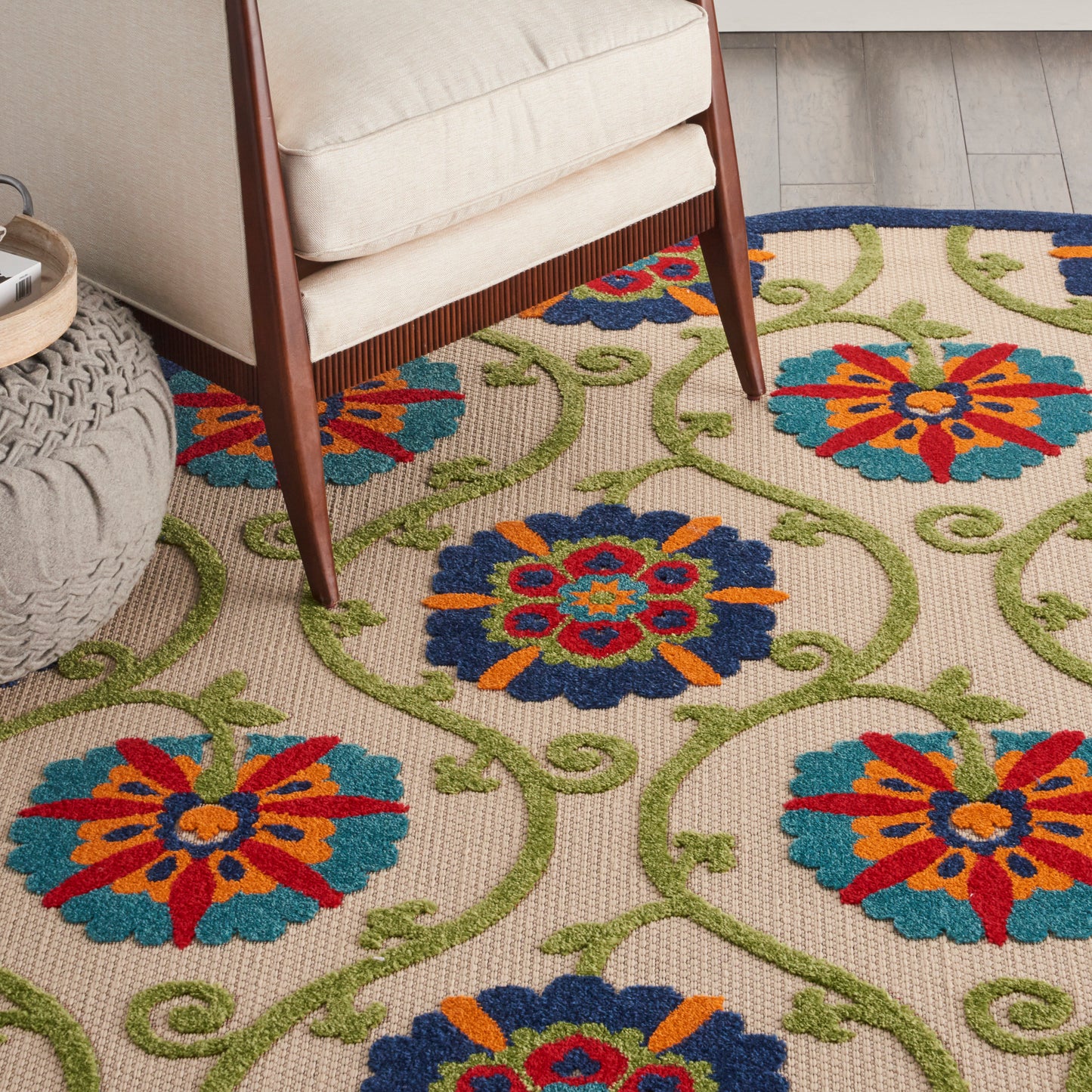 Colorful floral rug with blue and red medallion flowers, orange accents and green vines under a beige chair.