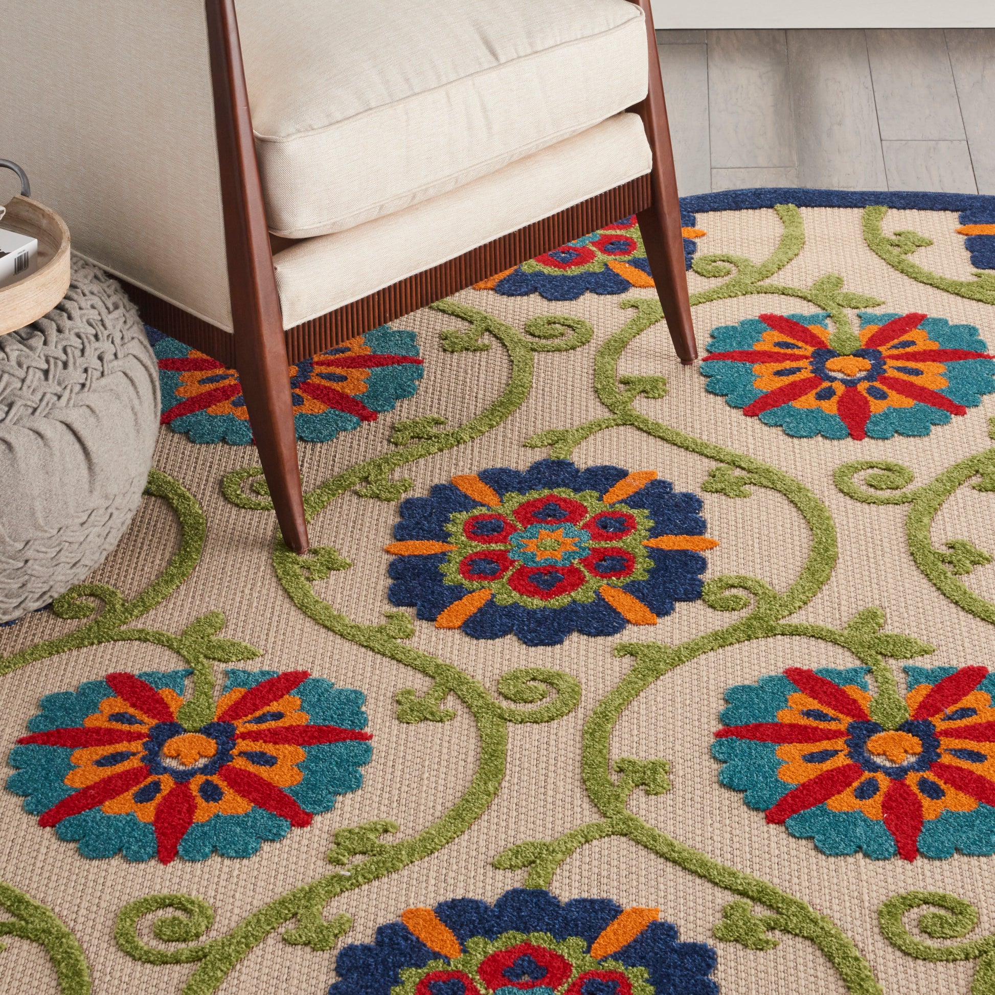 Colorful floral rug with blue and red medallion flowers, orange accents and green vines under a beige chair.