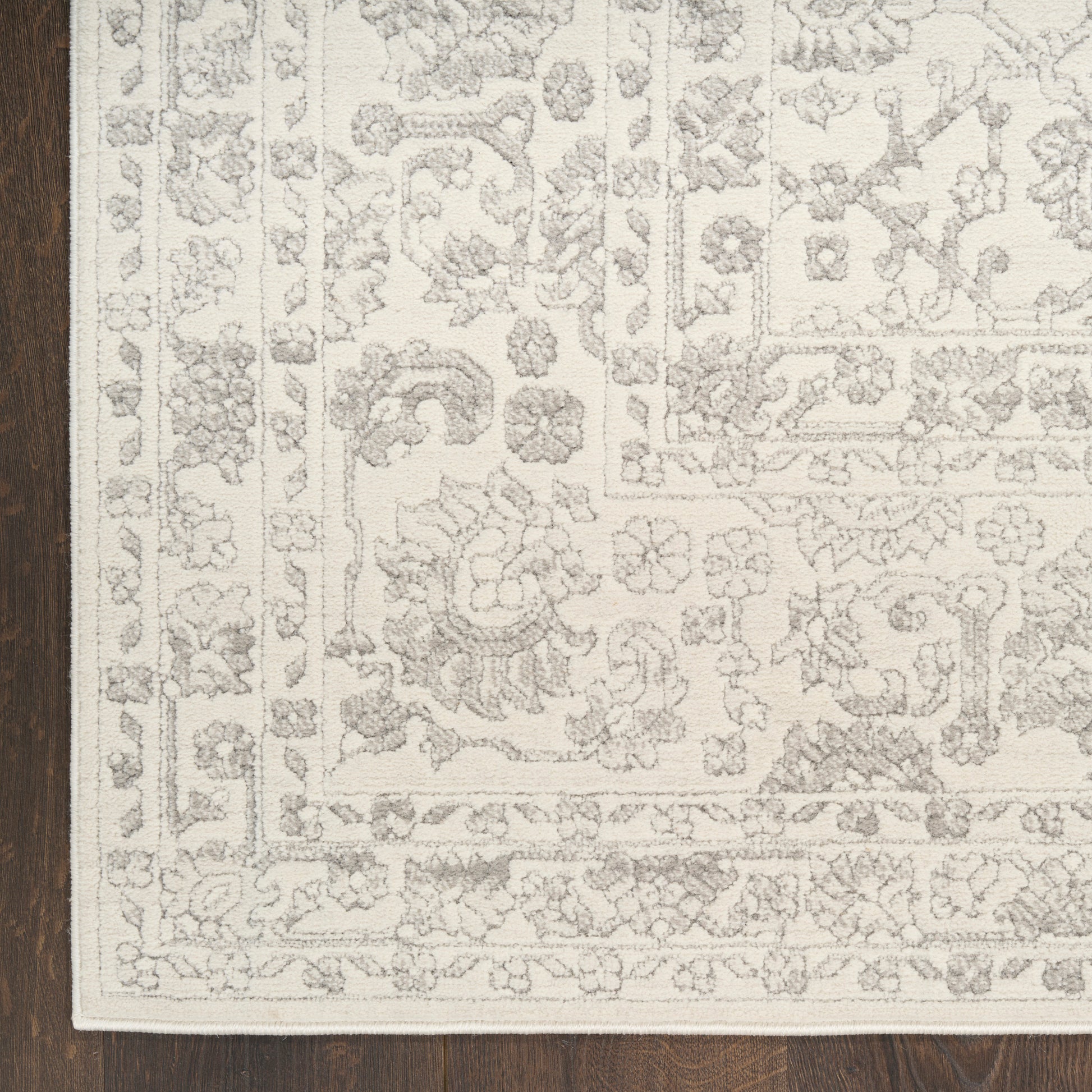 Cream oriental-style rug with a gray floral pattern and layered border on dark wood floor.