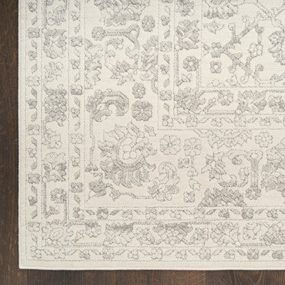 Cream oriental-style rug with a gray floral pattern and layered border on dark wood floor.
