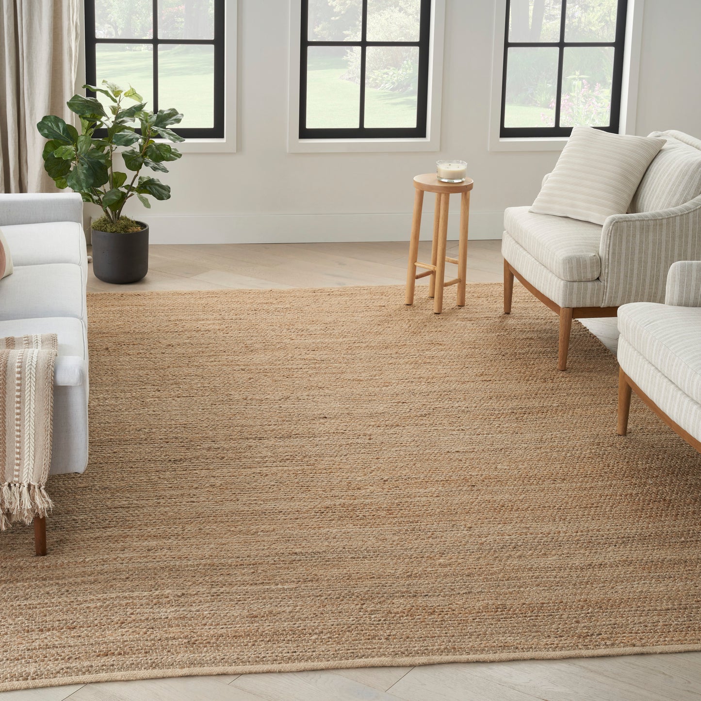 Neutral living room with a large natural jute rug, cream sofas, light wood legs, potted plant, and small wooden side table.