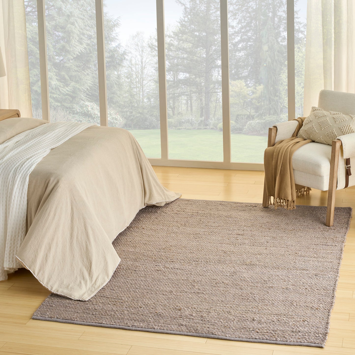 Beige duvet bed on light wood floor with a textured taupe rug; wooden chair with a throw beside a large window.