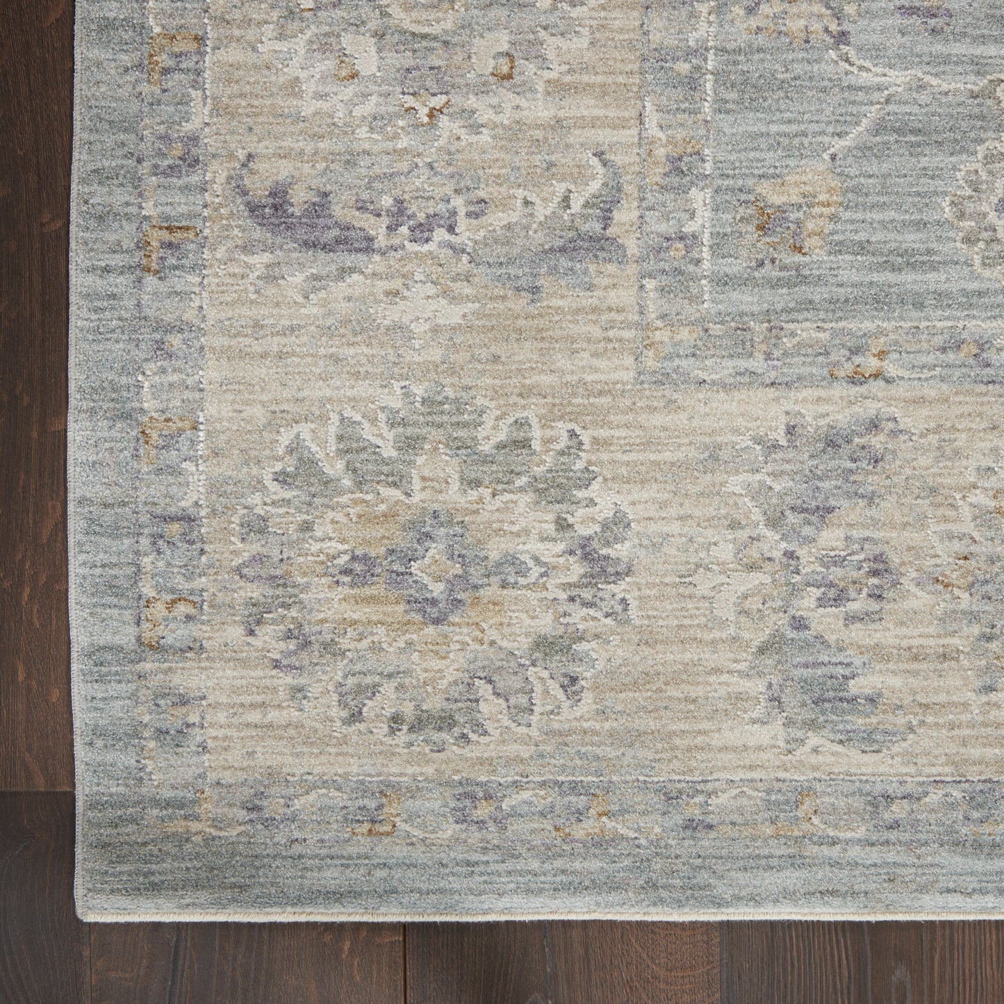 Distressed vintage-style area rug in soft blues and beiges with floral medallions on a dark wood floor.