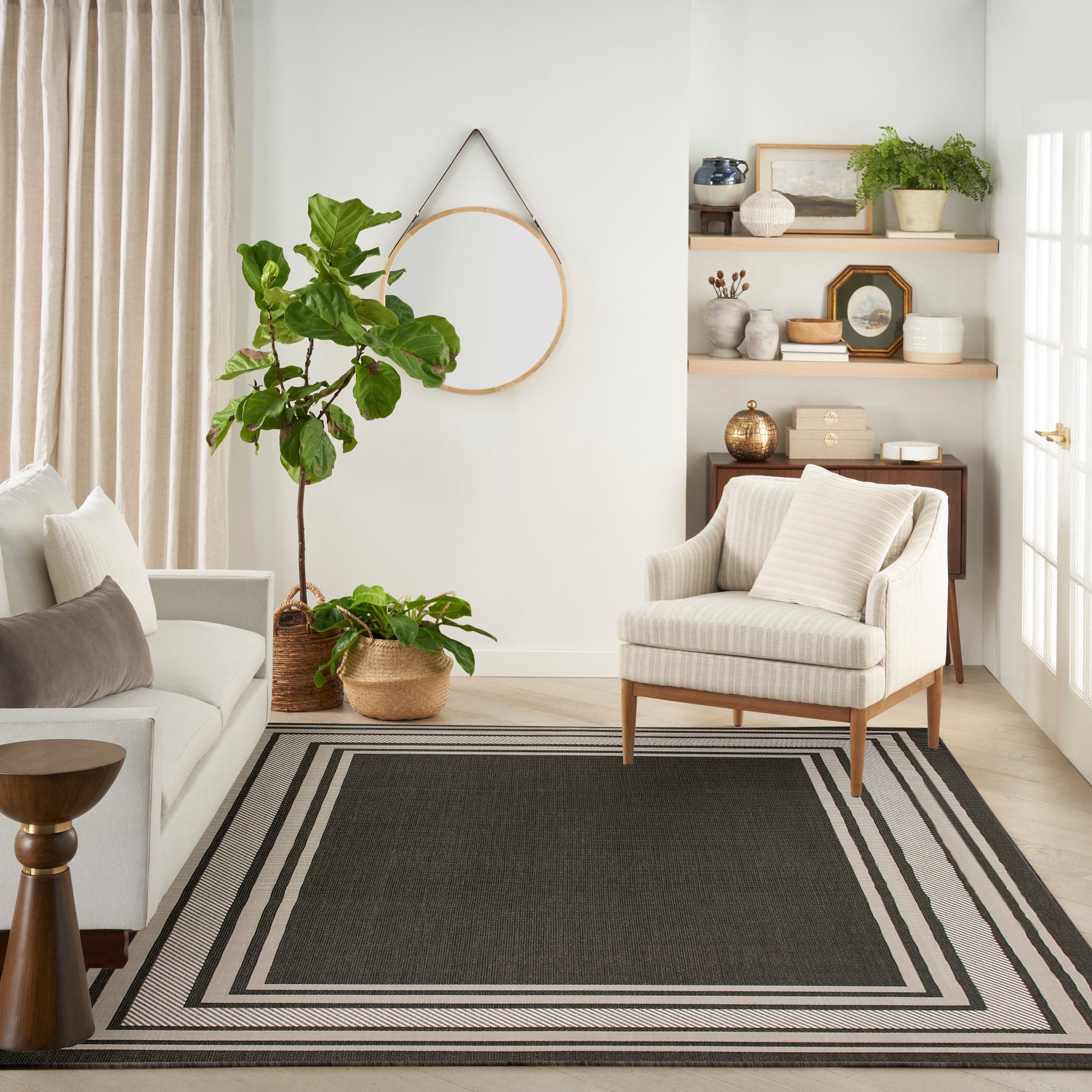 Cozy living room with beige sofa, striped rug, armchair, potted plants, circular wall hoop, and wooden shelves.