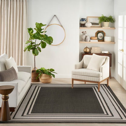 Cozy living room with beige sofa, striped rug, armchair, potted plants, circular wall hoop, and wooden shelves.