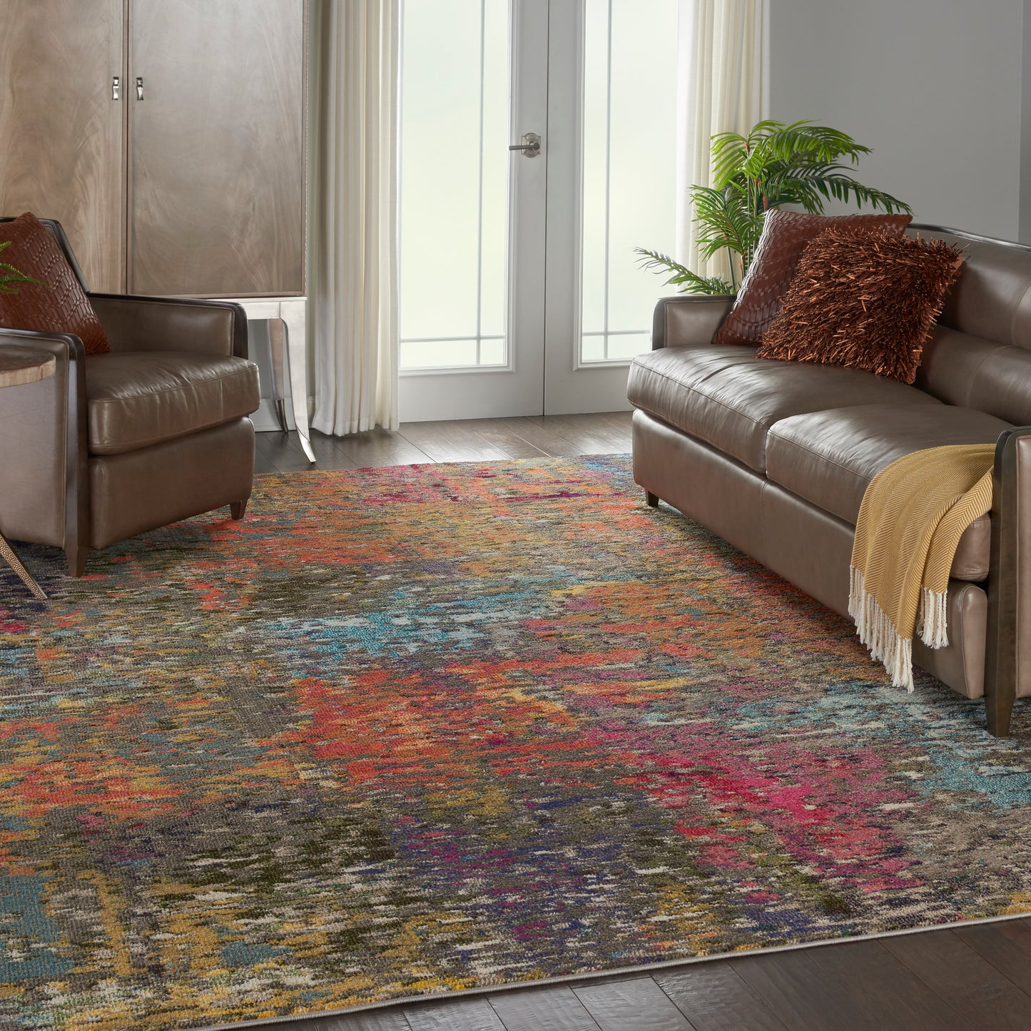 Living room with brown leather sofa and armchair, multicolor abstract rug, plant, pillows, and a yellow throw blanket.