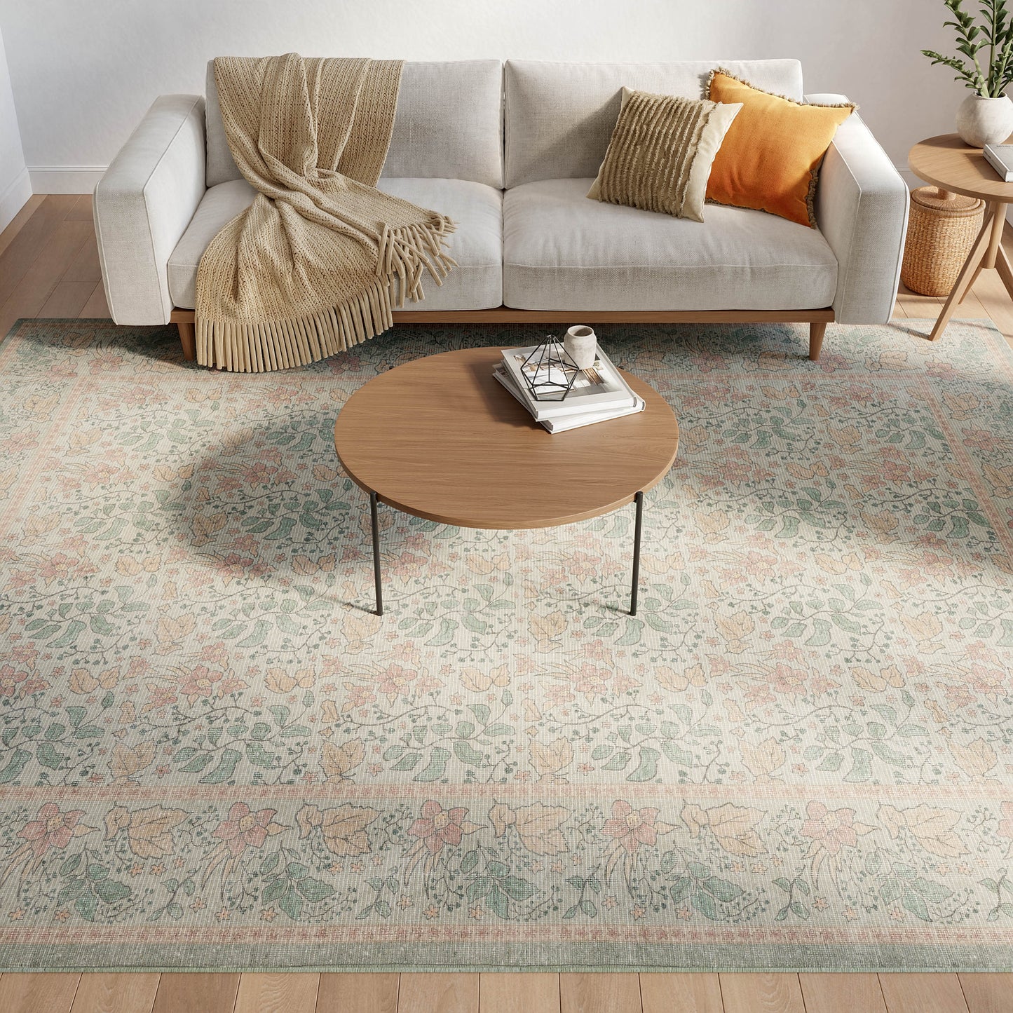Living room with a light gray sofa, beige throw, orange and tan cushions; round wood coffee table on a pastel floral rug.