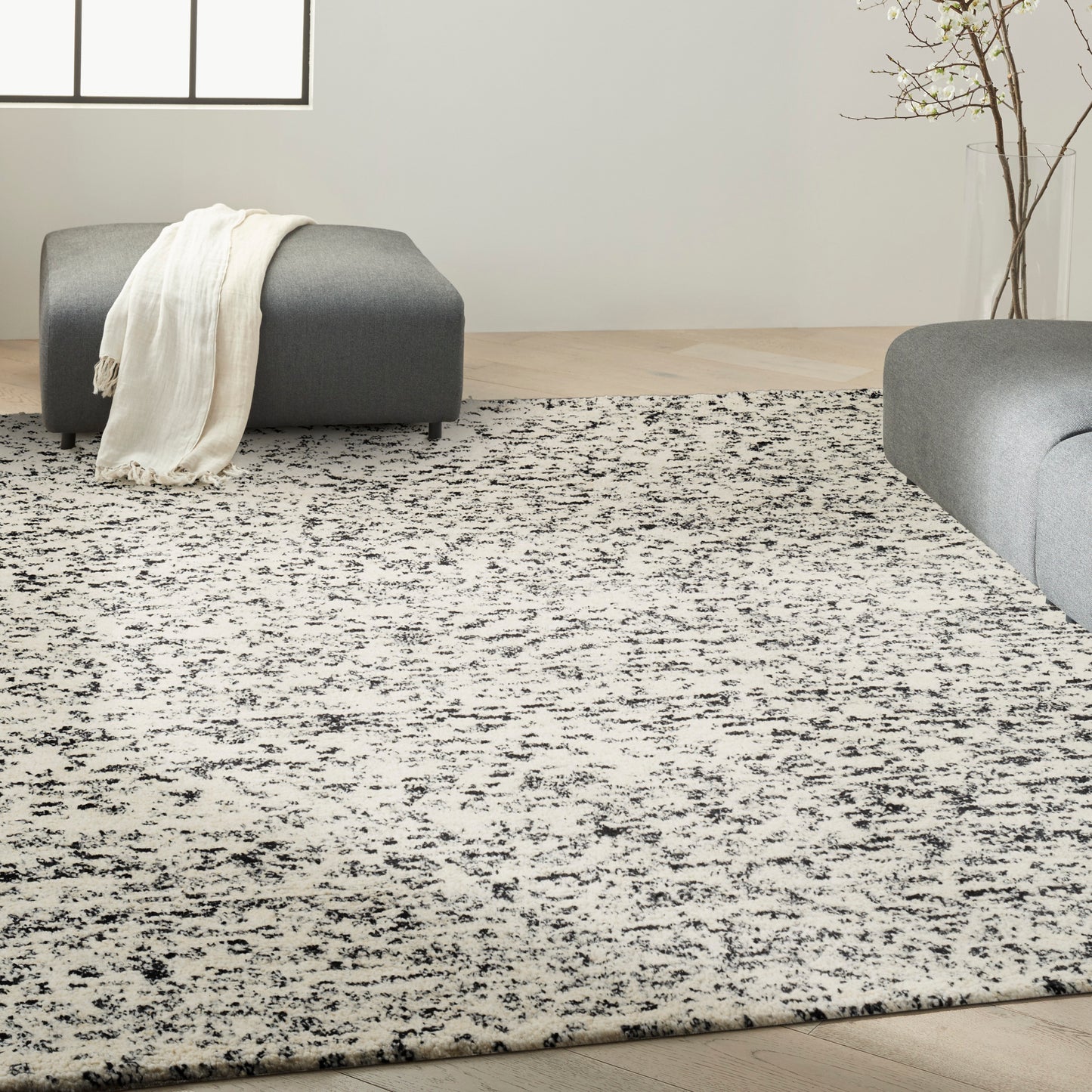 Large rectangular grayscale area rug with black speckled pattern in a modern living room with gray ottomans.