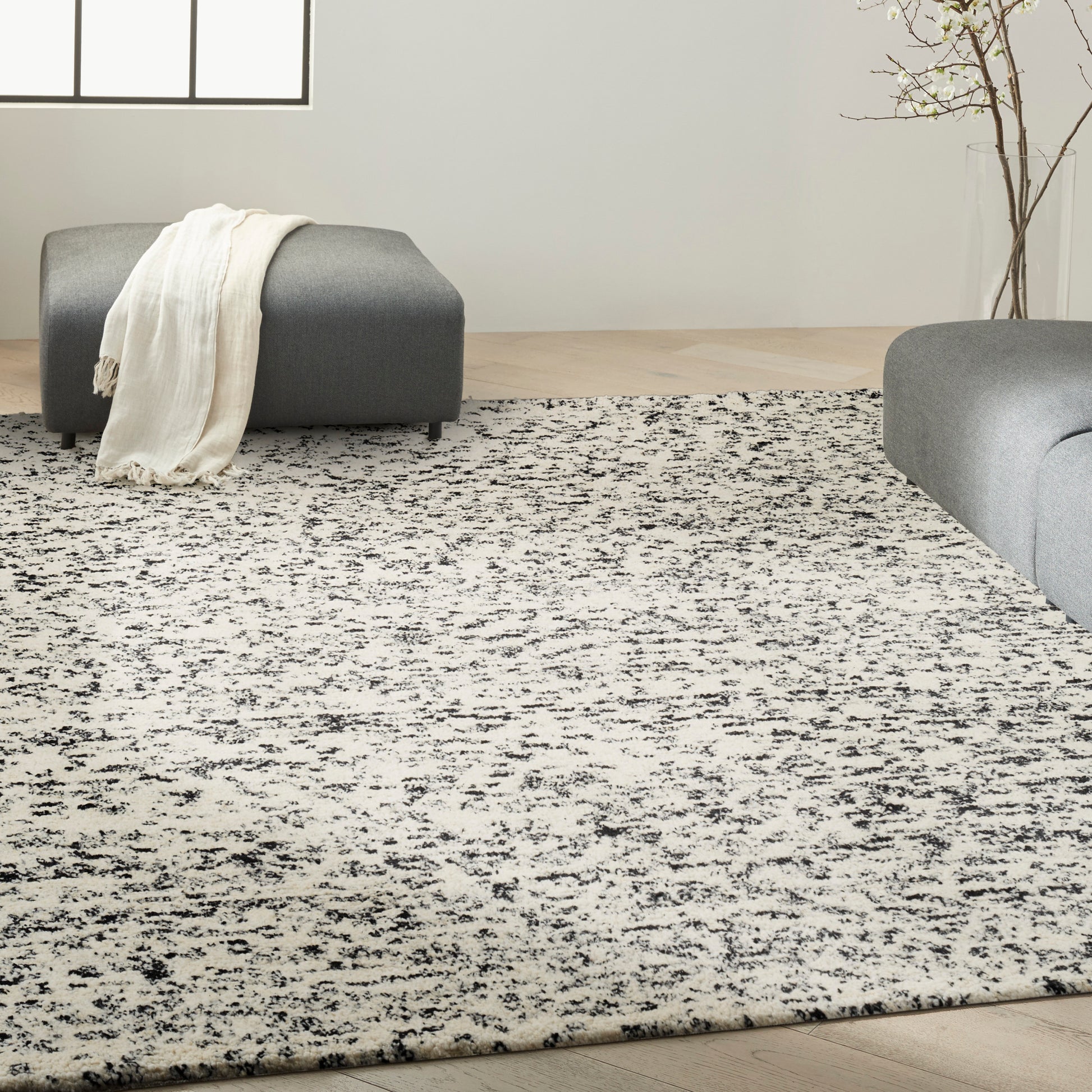 Large rectangular grayscale area rug with black speckled pattern in a modern living room with gray ottomans.