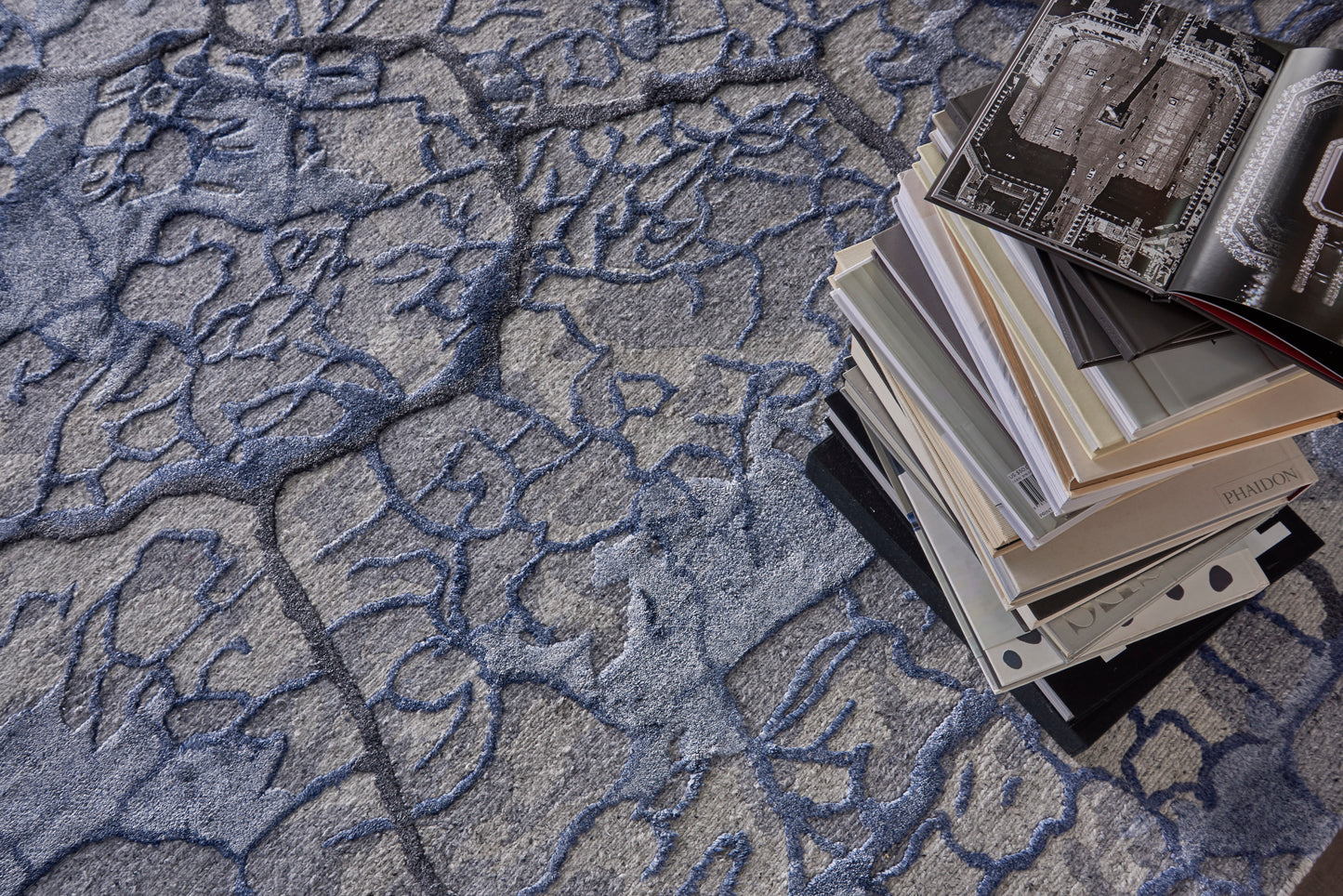Pile of art/design magazines with glossy pages on a blue abstract-patterned rug.