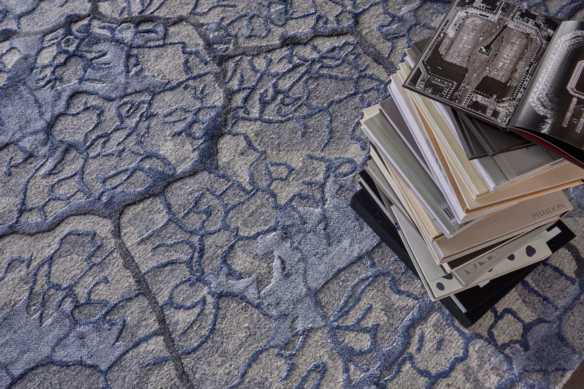 Pile of art/design magazines with glossy pages on a blue abstract-patterned rug.