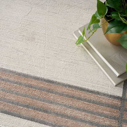 Cream textured rug with brown and gray striped border; stack of books topped by a green plant in a gold pot.