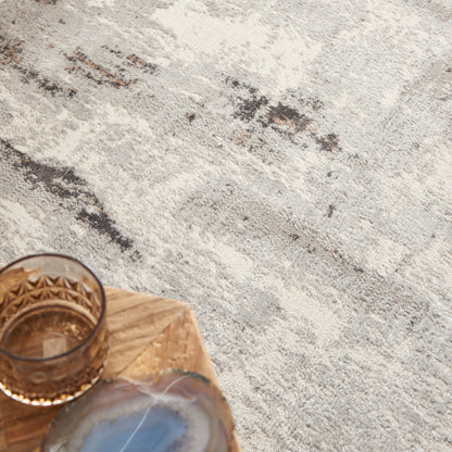 Amber whiskey in a faceted brown glass tumbler on a light wood cutting board atop a textured gray surface.