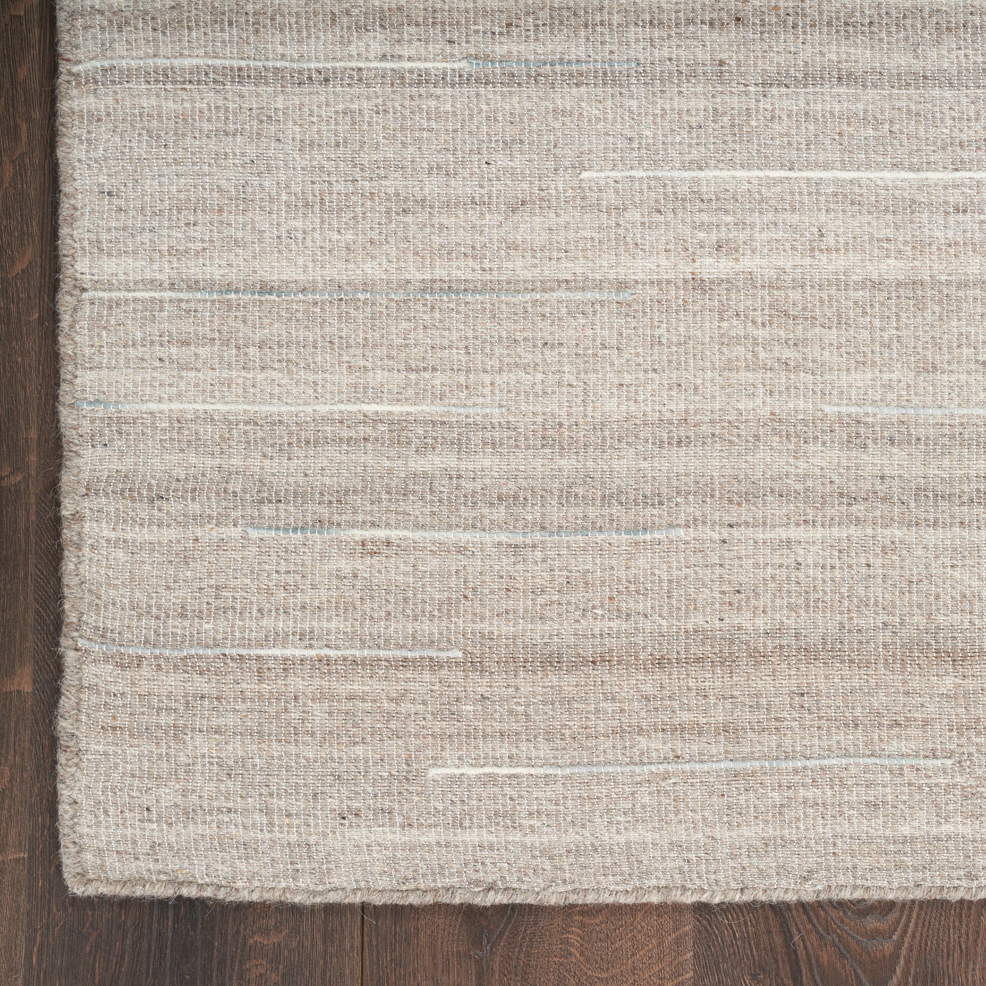 Natural beige woven rug with subtle blue flecks on dark wood floor; rectangular, textured jute-cotton blend.