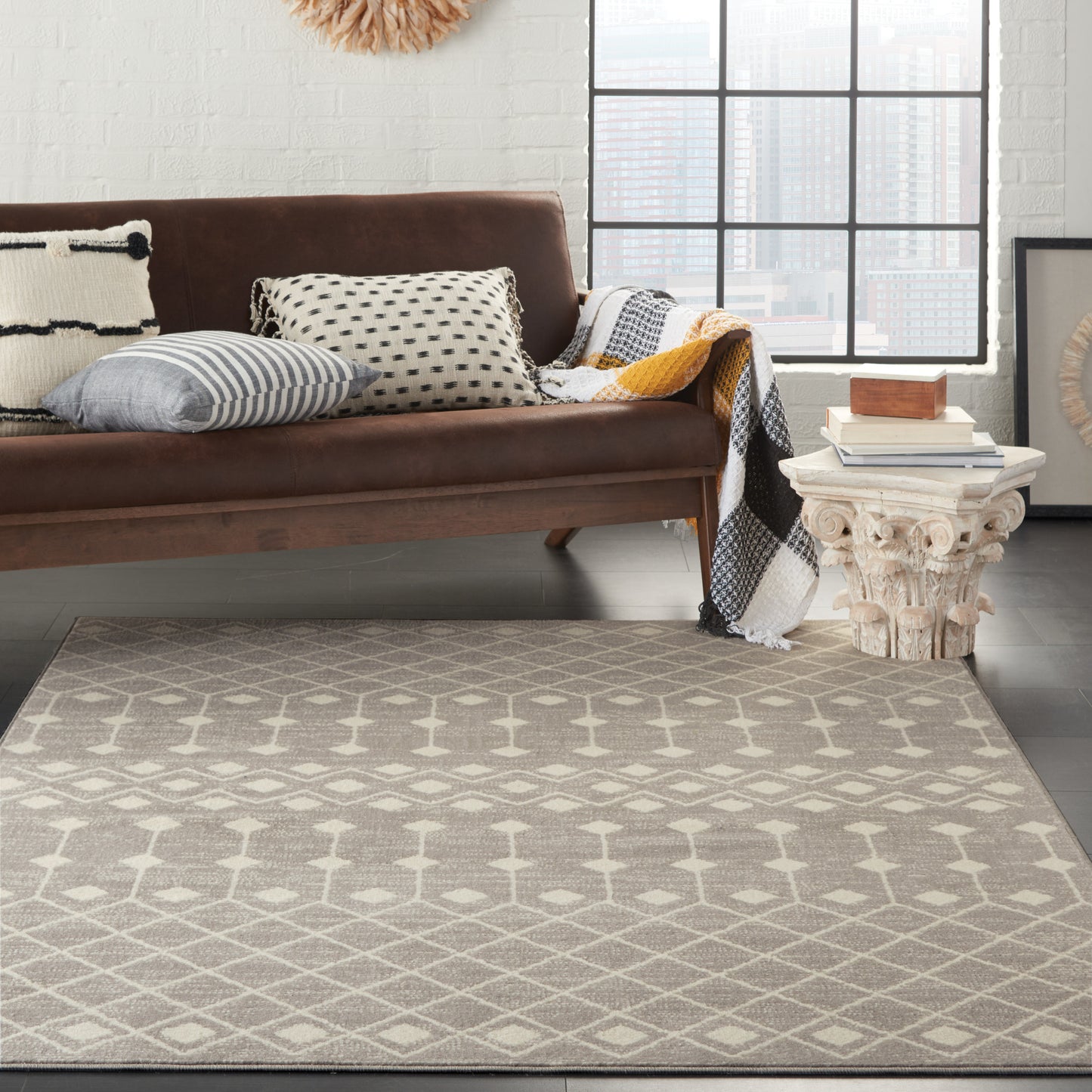 Brown sofa with patterned cushions, light gray geometric rug, white carved side table with books in bright living room