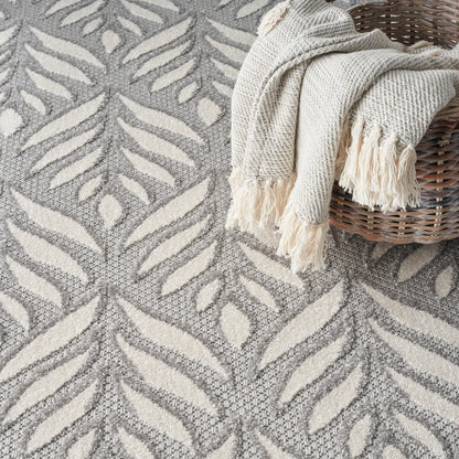 Grey and cream leaf-pattern rug with a cream fringed knit throw draped over a wicker basket.