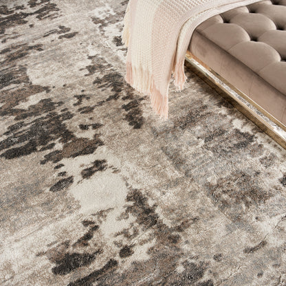 Abstract charcoal gray and beige distressed area rug beside a tufted beige velvet sofa with gold trim and a blush throw.