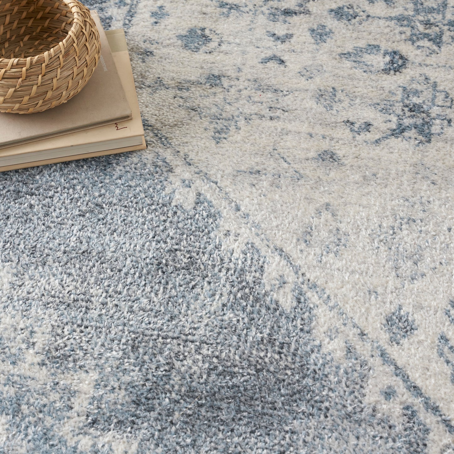 Woven rattan basket atop a stack of papers on a blue and cream patterned rug.