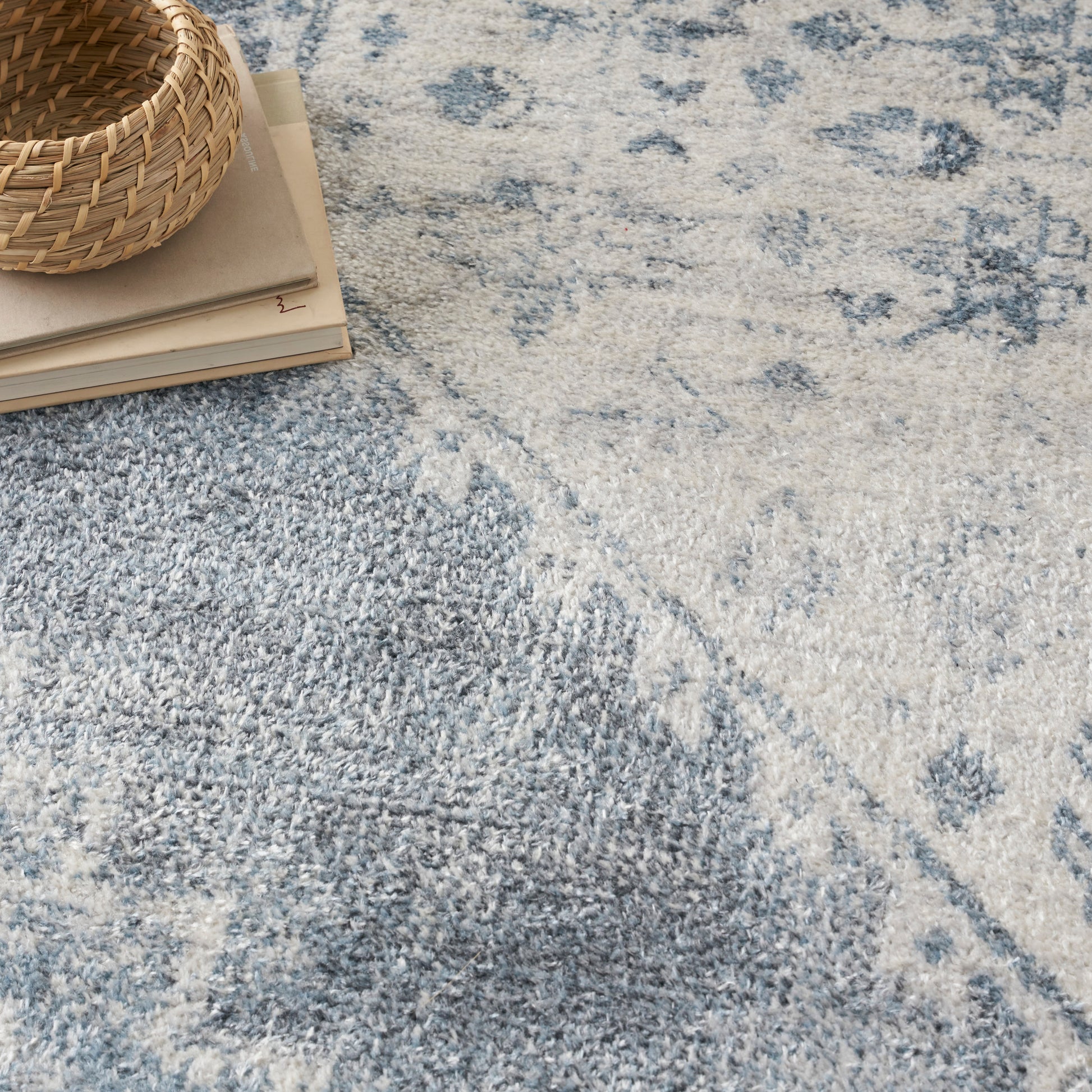 Woven rattan basket atop a stack of papers on a blue and cream patterned rug.
