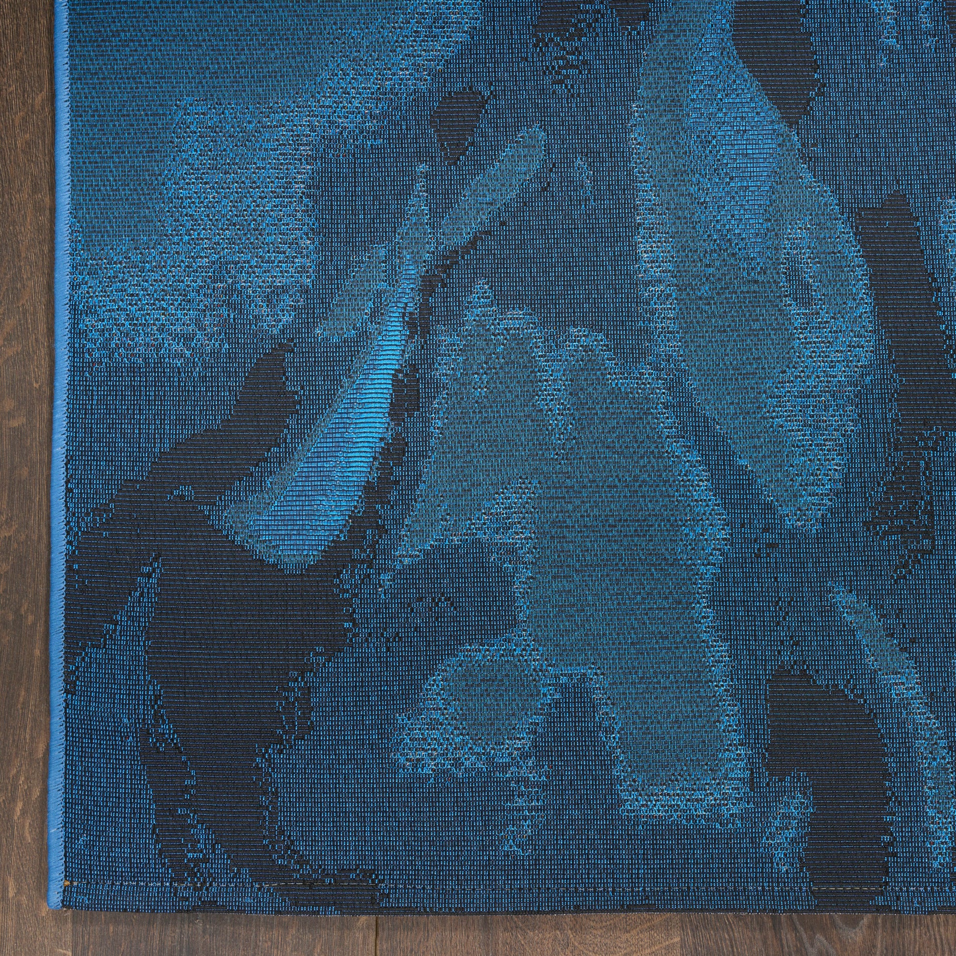 Rectangular blue area rug, 5' x 7', with a dark navy floral/abstract pattern and woven texture on a wood floor.
