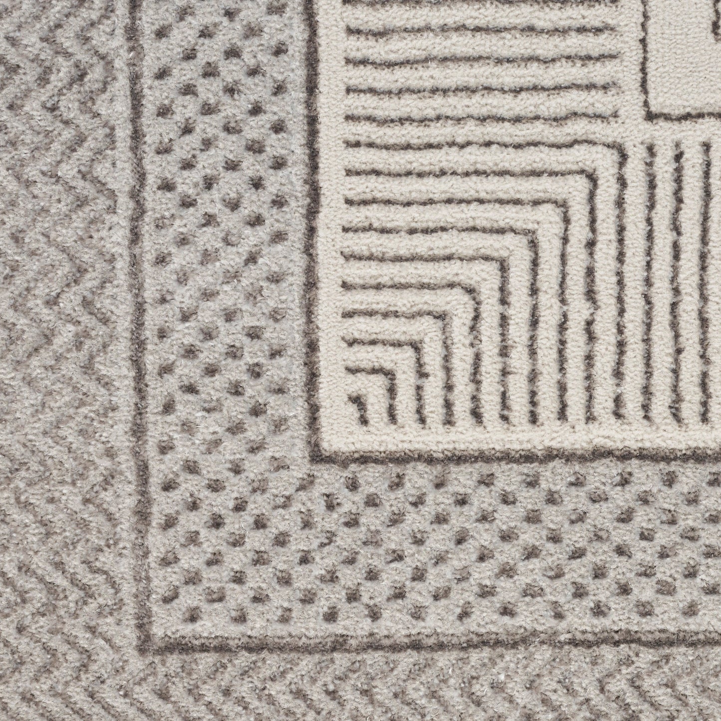 Close-up of a gray and ivory rug with a dotted border, zigzag edge, and stepped square corner pattern.