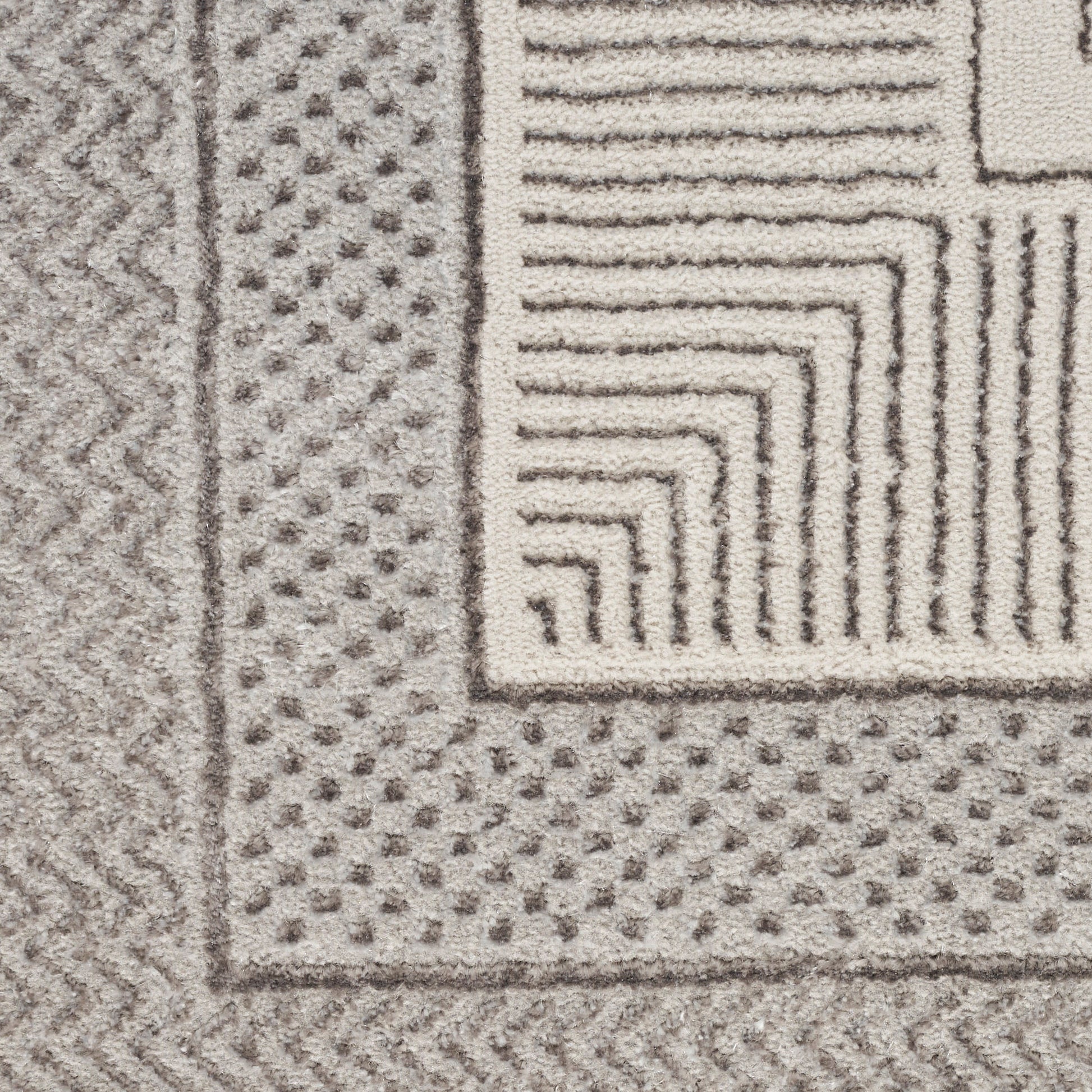 Close-up of a gray and ivory rug with a dotted border, zigzag edge, and stepped square corner pattern.
