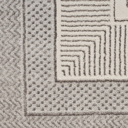 Close-up of a gray and ivory rug with a dotted border, zigzag edge, and stepped square corner pattern.