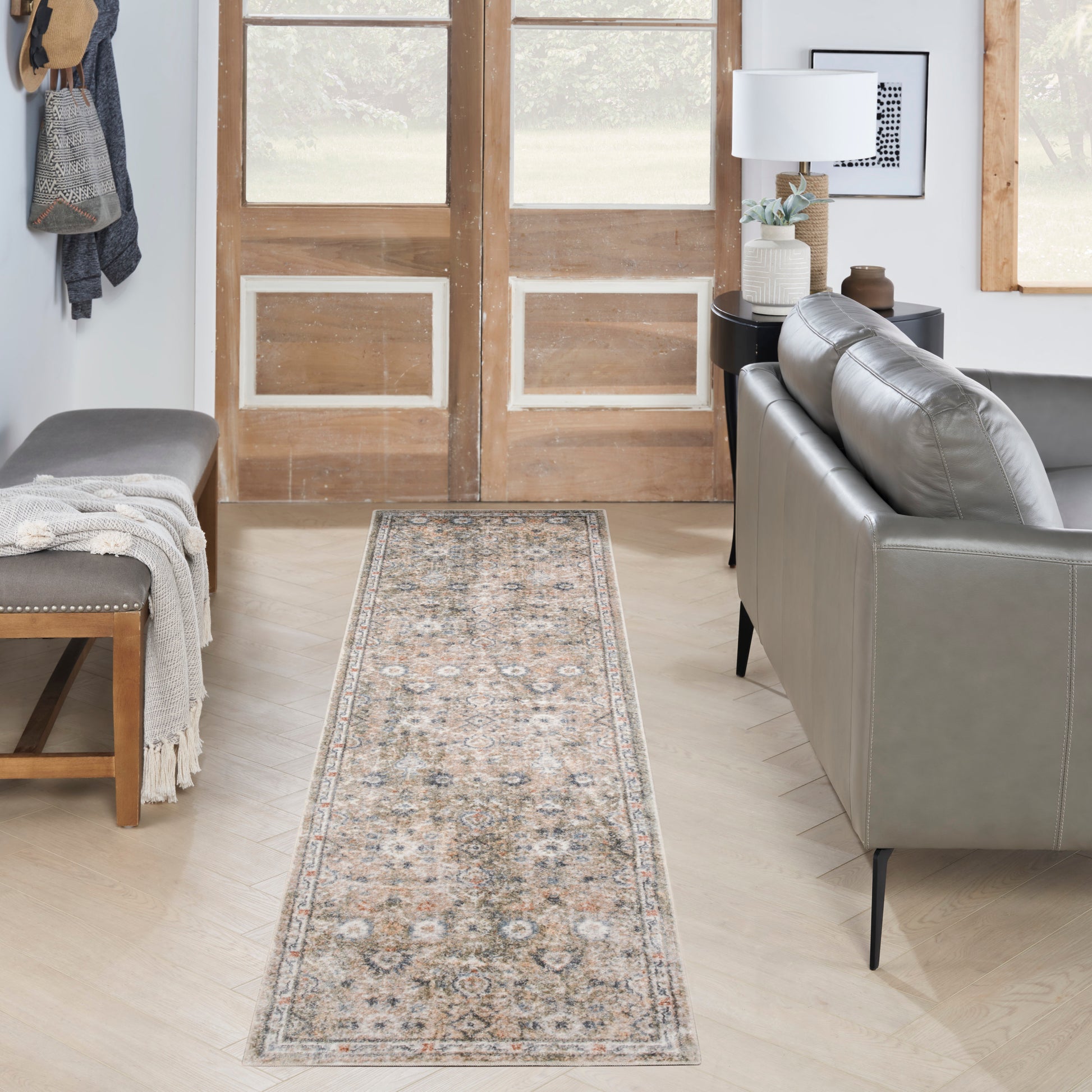 Narrow Persian-style floral runner rug in beige, blue & rust on light wood floor beside a gray sofa.